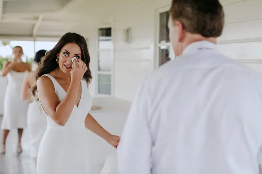 Bride wiping her eye while facing a man on the veranda
