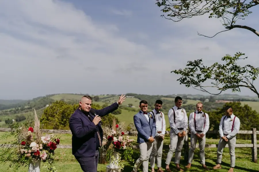 Celebrant gesturing beside the groom and groomsmen at a hilltop ceremony
