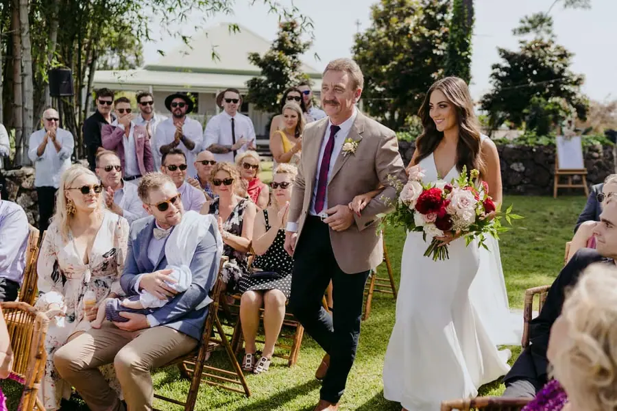 Bride entering the garden ceremony beside a man in a tan suit