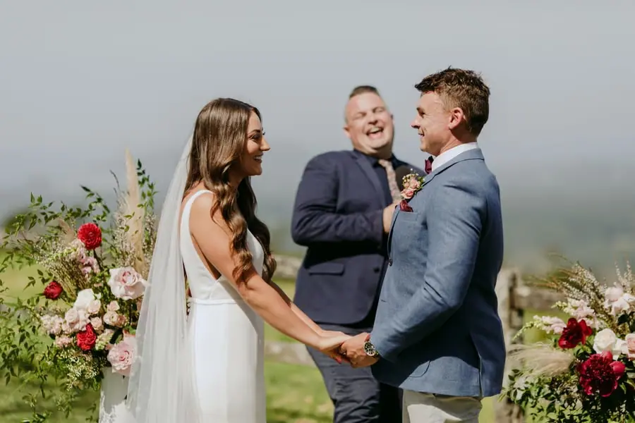 Bride and groom holding hands and laughing beside the celebrant
