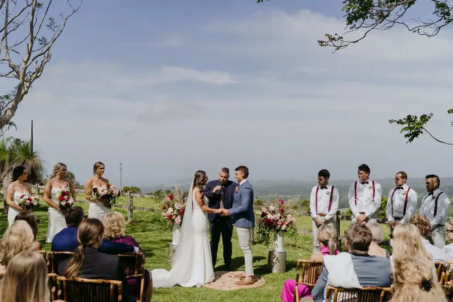 Wide view of the wedding party and guests at a ceremony overlooking green hills