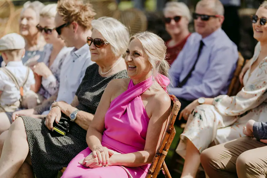 Seated guests smiling in sunglasses and bright clothes during the ceremony