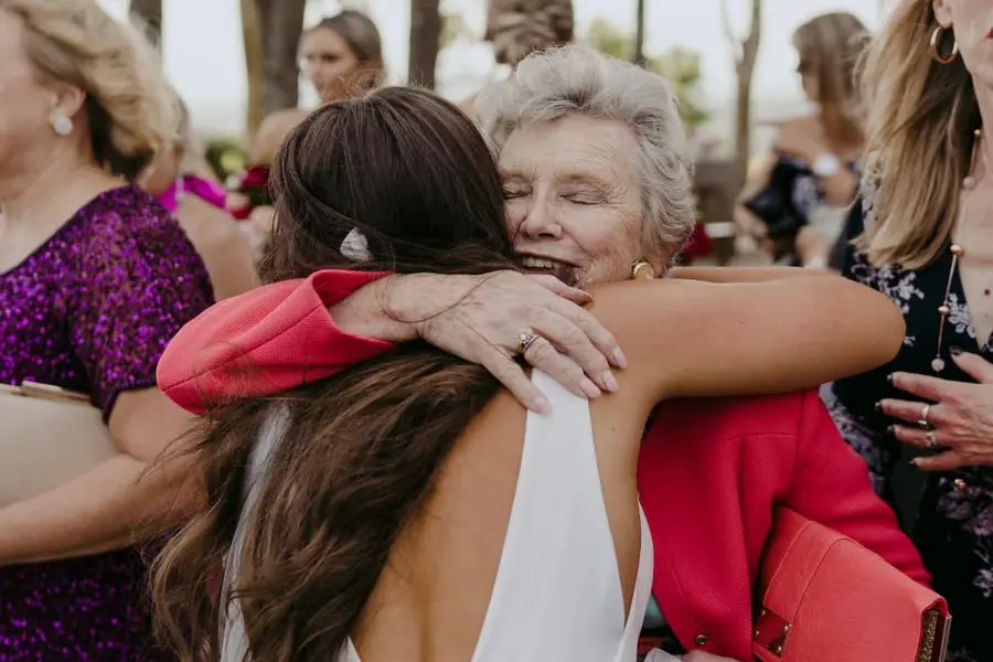 Bride hugging a grey-haired woman in a red jacket