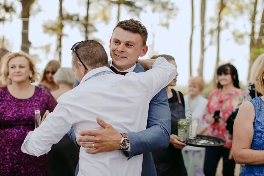 Groom smiling as he hugs a guest in a white shirt