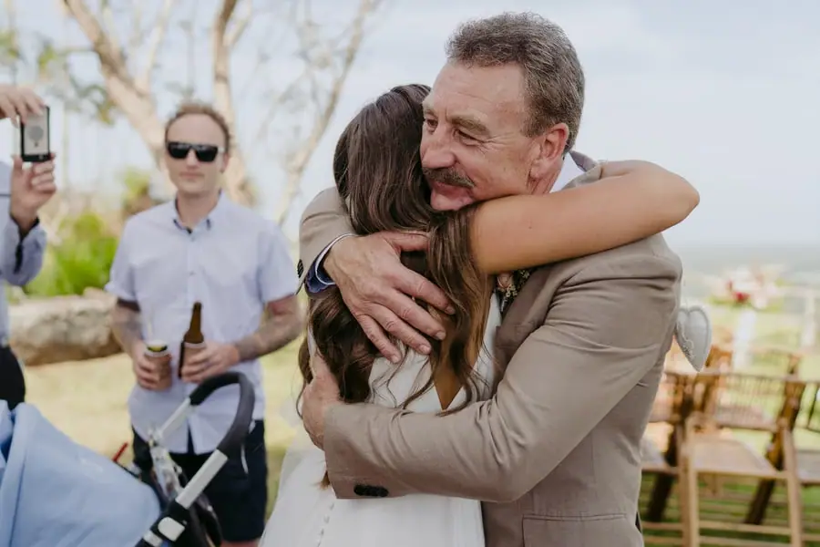 Bride hugging a smiling man in a tan suit outdoors