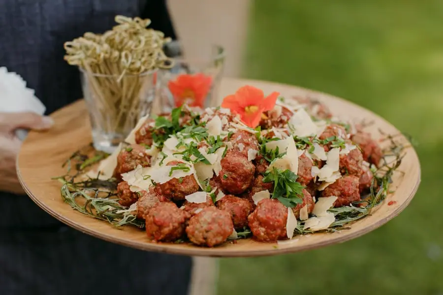 Platter of bite-sized savoury food topped with herbs beside wooden skewers