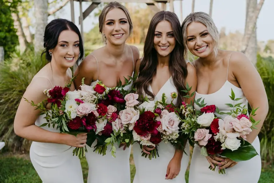 Bride and three bridesmaids smiling together with burgundy and pale bouquets