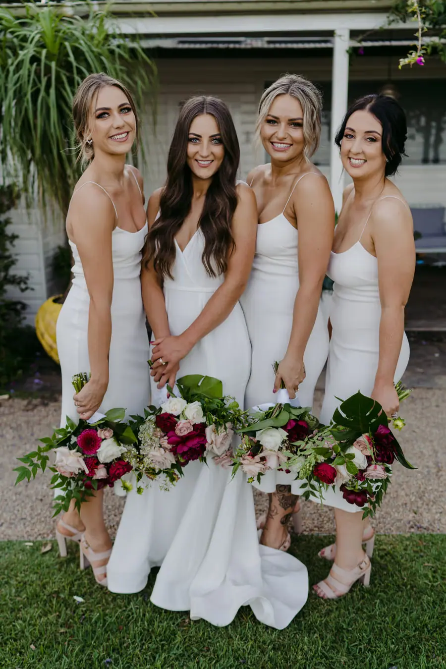 Bride and bridesmaids standing together in white dresses with bouquets