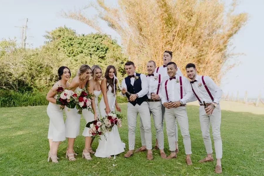 Wedding party laughing together on a sunlit lawn with drinks