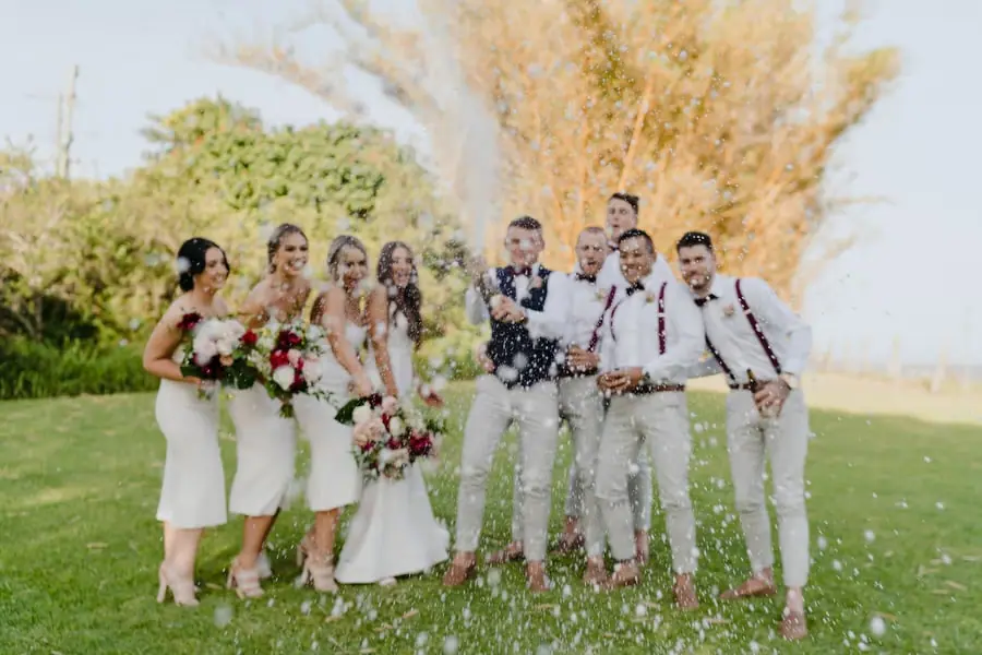 Wedding party celebrating as sparkling wine sprays across the lawn