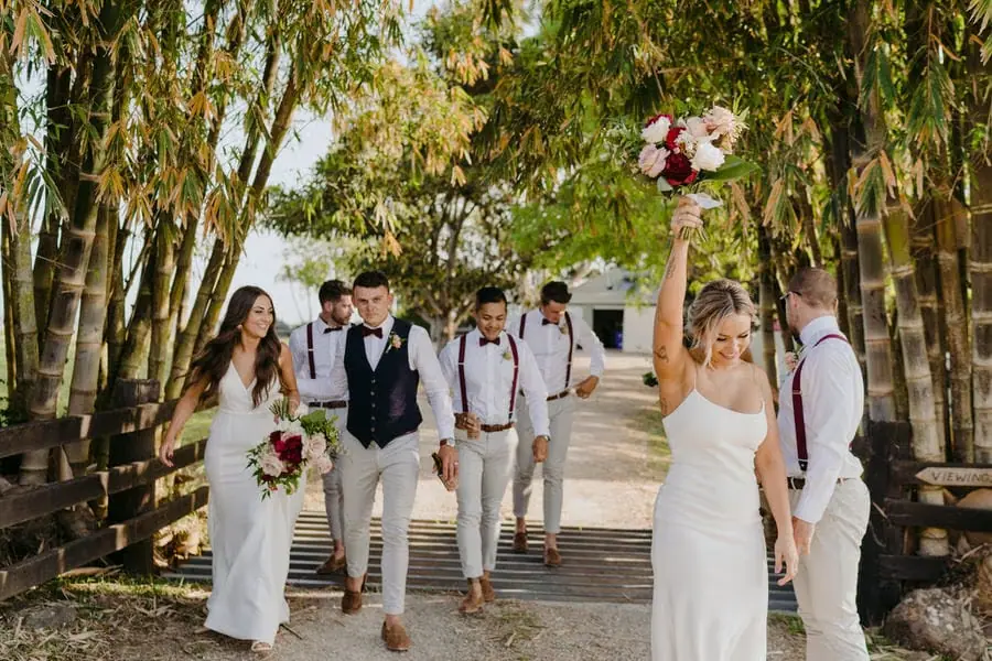 Wedding party walking over a wooden bridge beneath bamboo branches