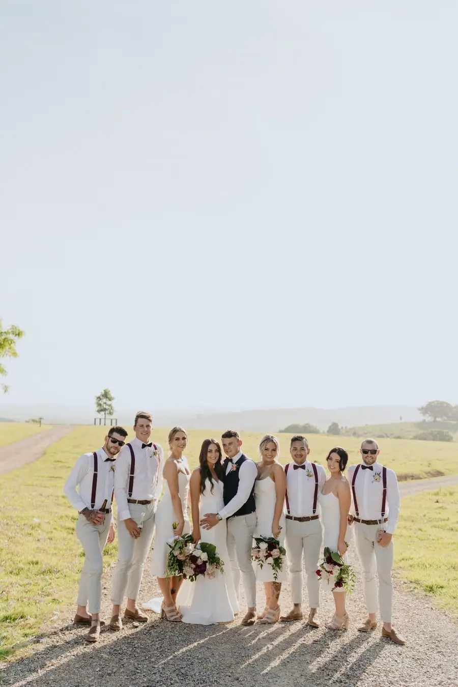 Wedding party posing together on a country lane beside open fields
