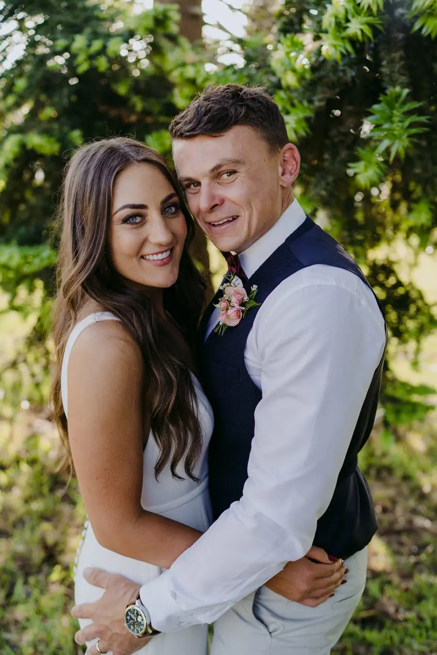 Bride and groom embracing beneath leafy trees