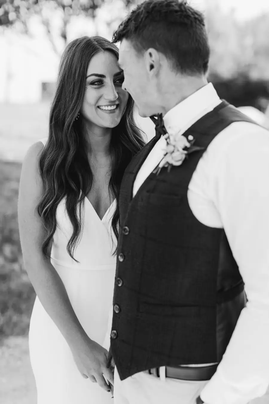 Black and white photograph of the bride and groom smiling at each other outdoors