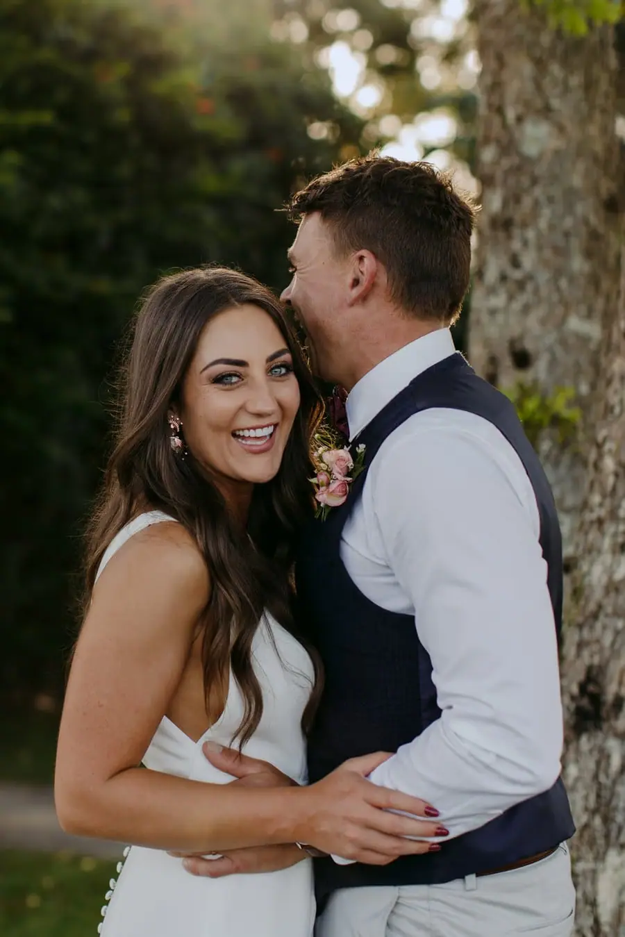 Groom kissing the bride's forehead as she smiles toward the camera