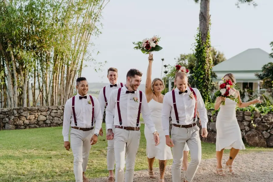 Wedding party walking across a lawn while raising bouquets