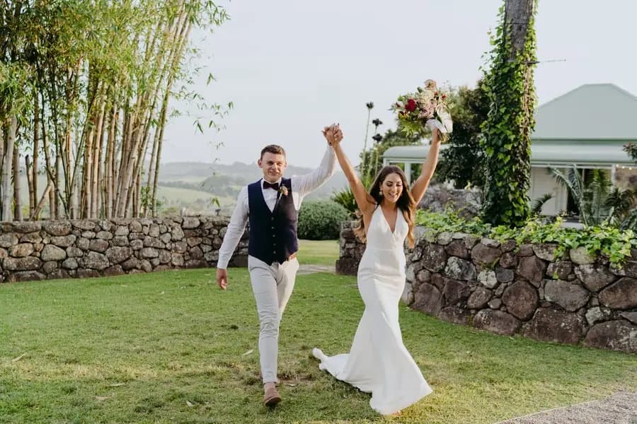 Bride raising her bouquet as the groom lifts their joined hands outside the reception