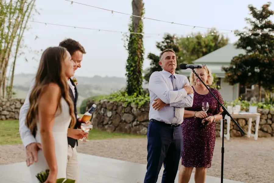 Man speaking into a microphone beside a woman as the couple listen outdoors