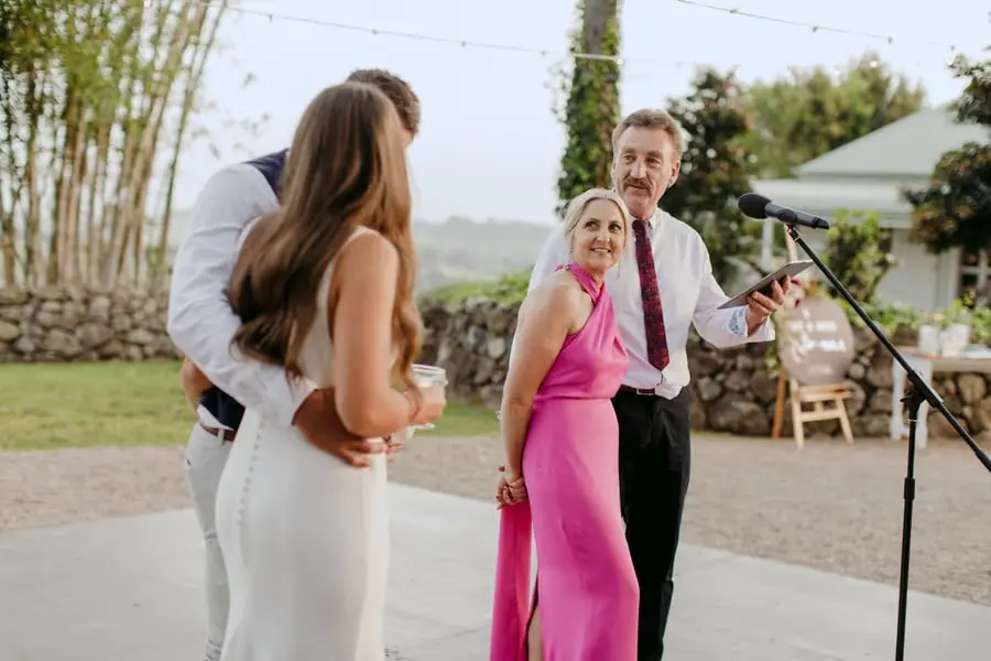 Man in a burgundy tie speaking beside a woman in a bright pink dress