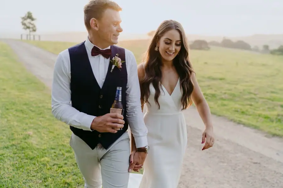 Bride and groom holding hands and smiling along a sunlit lane