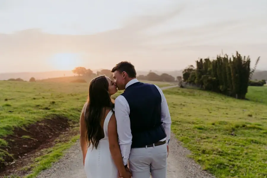 Bride and groom leaning toward each other on a country lane in golden evening light