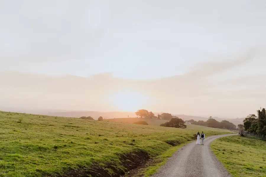 Wide view of the couple walking along a winding country lane at sunset