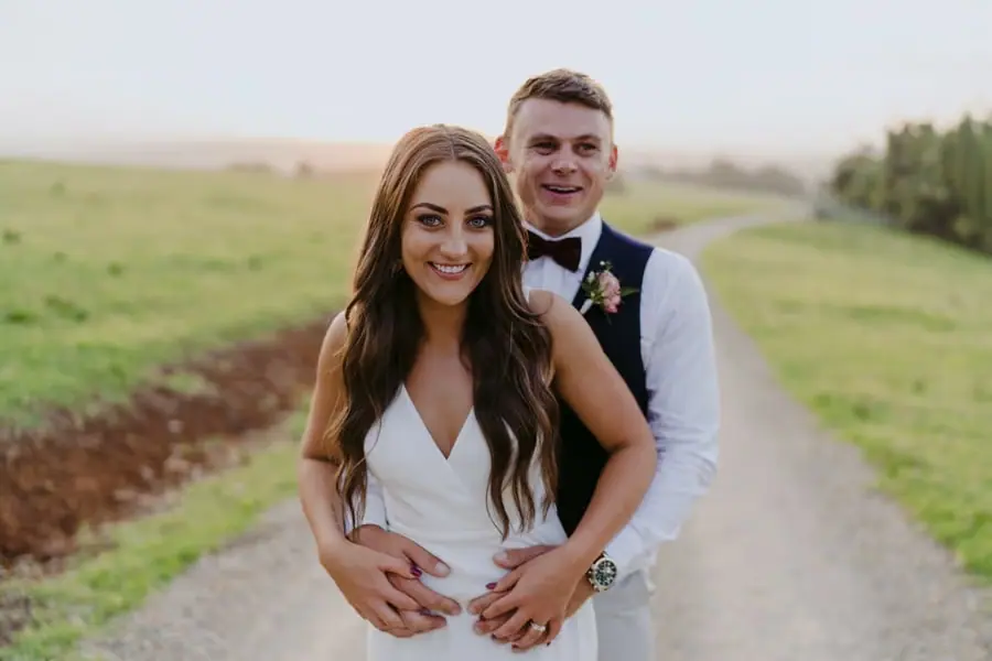Groom embracing the smiling bride from behind on a country lane