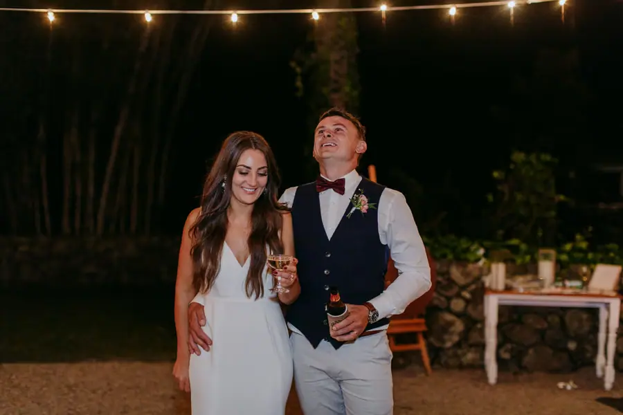Bride and groom laughing together beneath festoon lights at night