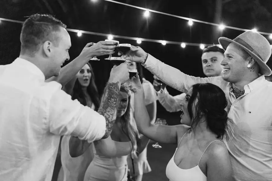 Black and white photograph of guests raising their glasses together outdoors at night