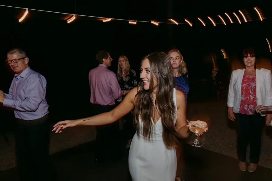 Bride dancing with a drink in her hand beneath outdoor lights