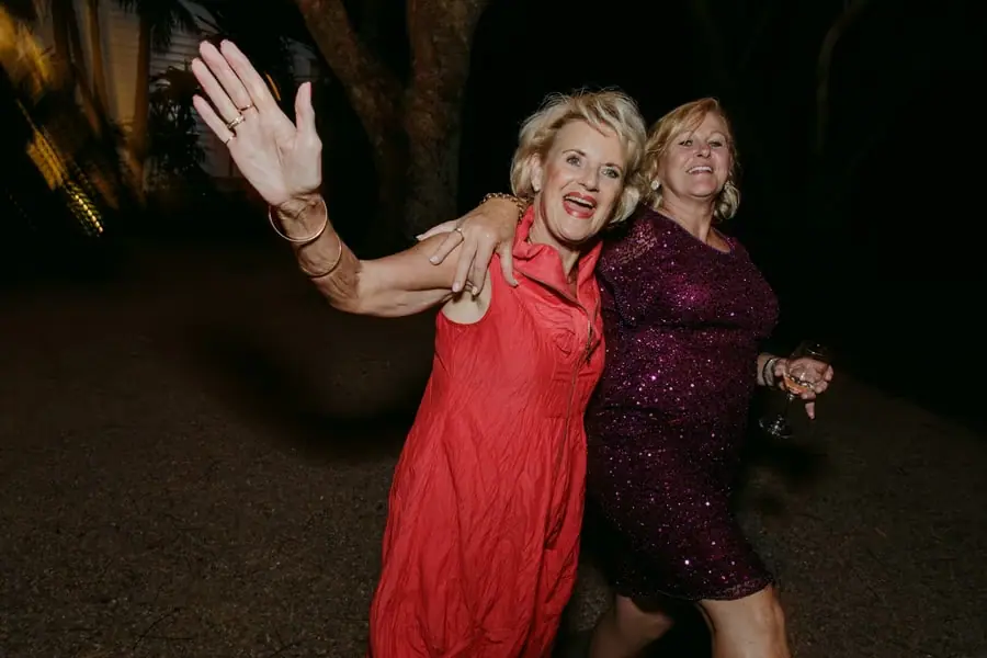 Two women laughing and dancing together with one waving toward the camera