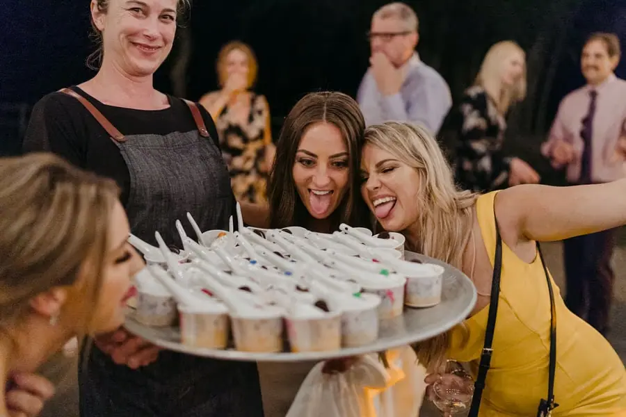 Bride and a guest leaning toward a server's tray of small dessert cups