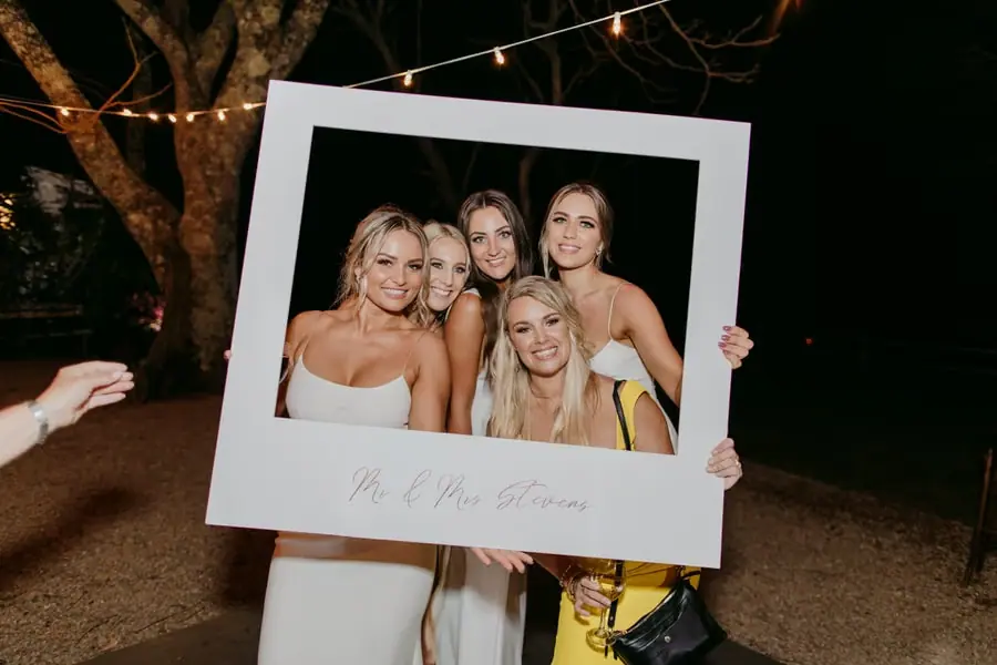 Five women smiling together through a large white photo frame