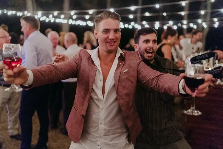 Guest holding two glasses outward beside a smiling friend on the dance floor