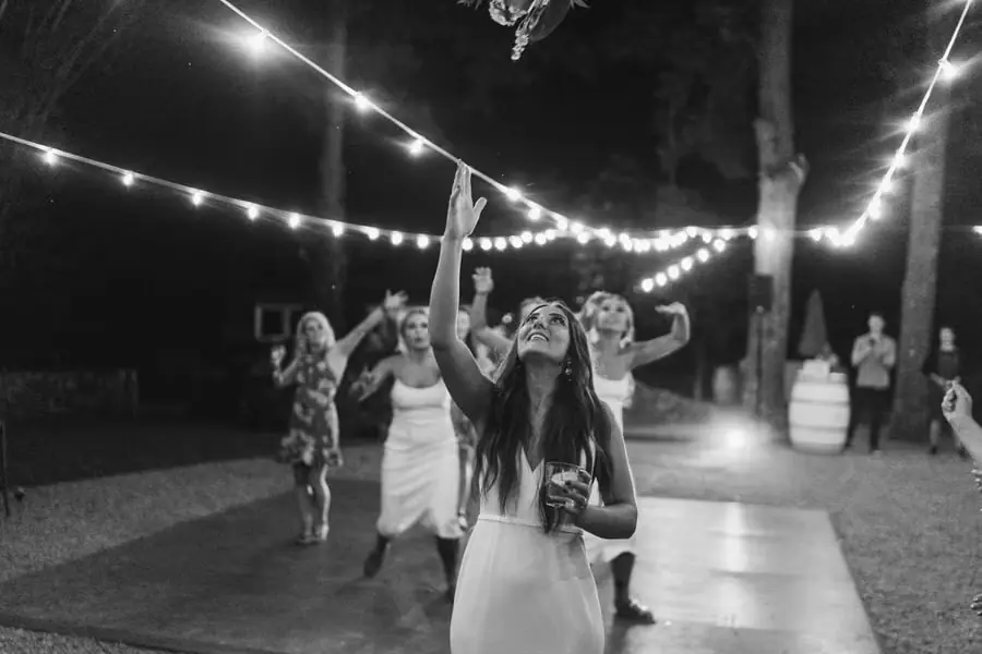 Black and white photograph of women reaching toward a bouquet in the air
