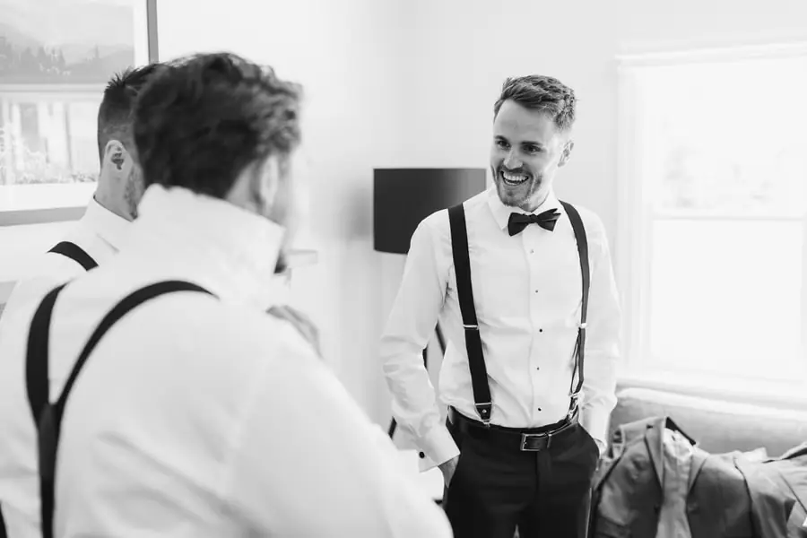 Black-and-white photograph of men smiling together in shirts and braces while getting ready
