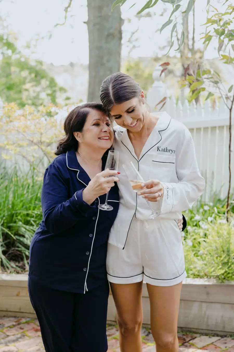 Bride leaning her head against a woman as they hold champagne glasses