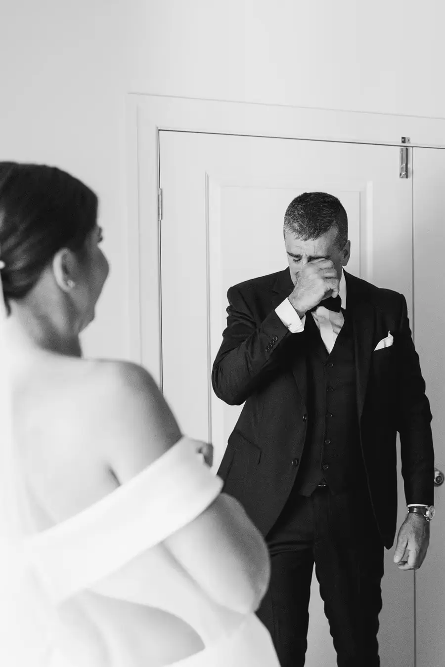 Black-and-white photograph of an older man wiping his eye as he sees the bride
