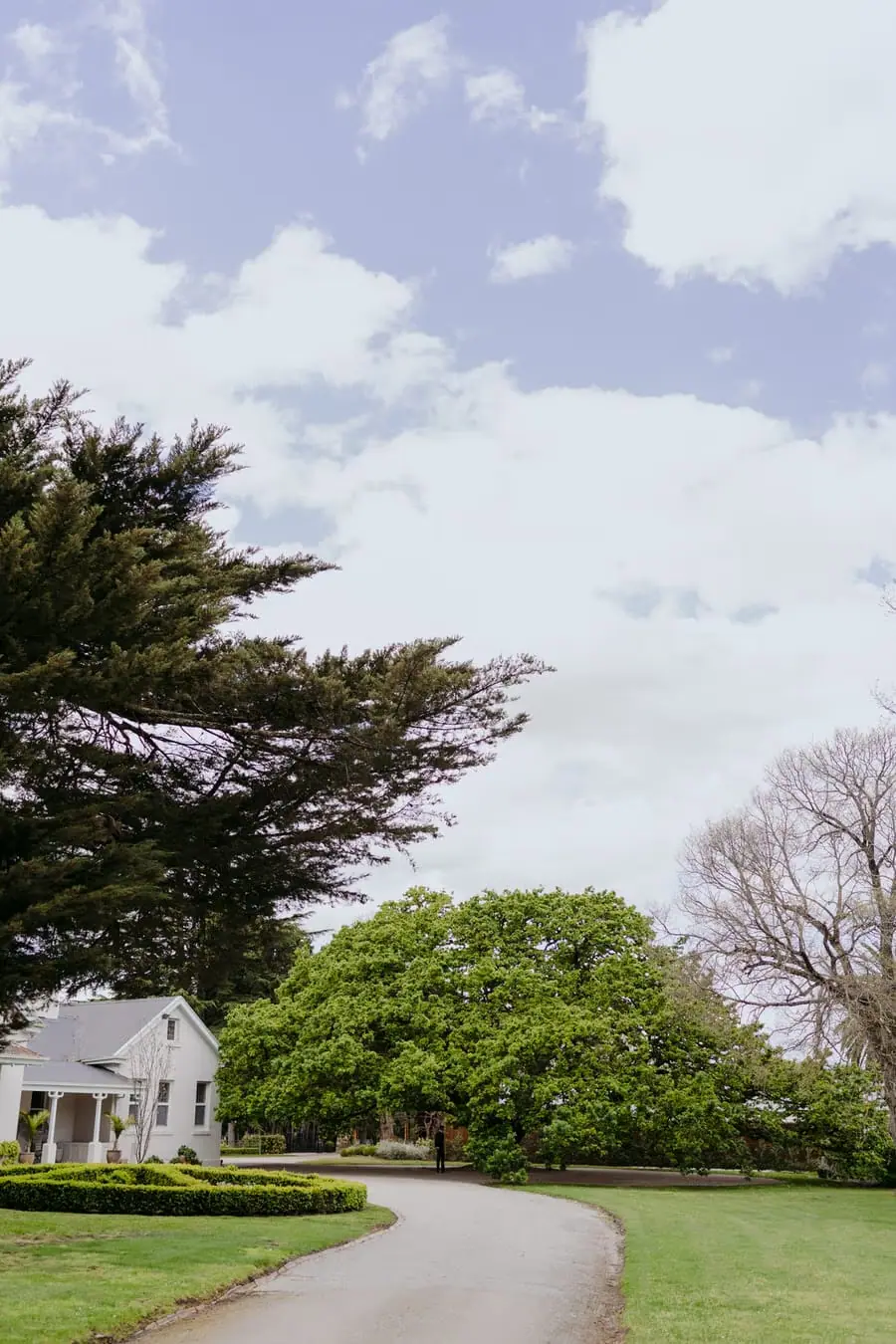Curving driveway leading past lawns and a white garden building