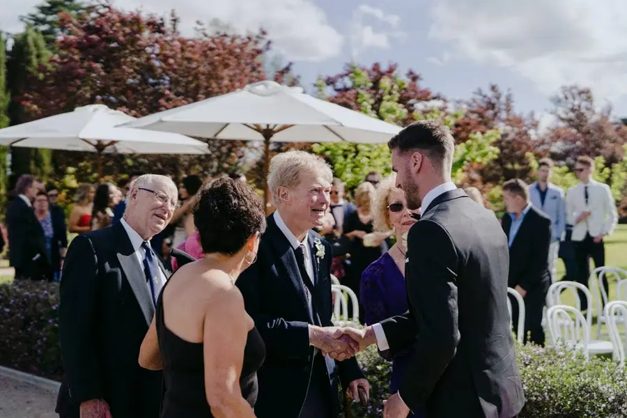 Groom greeting guests among white ceremony chairs in a garden