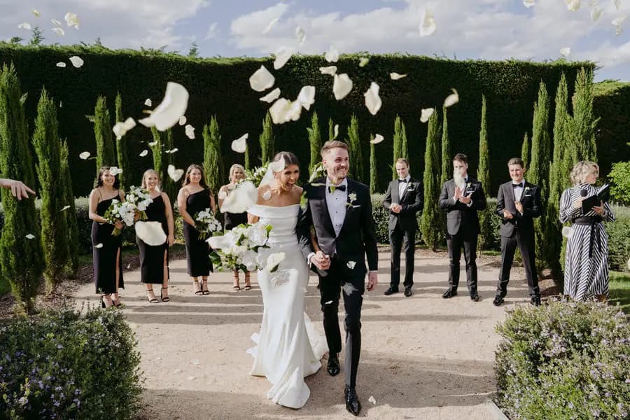 Guests throwing white petals over the bride and groom as they walk together