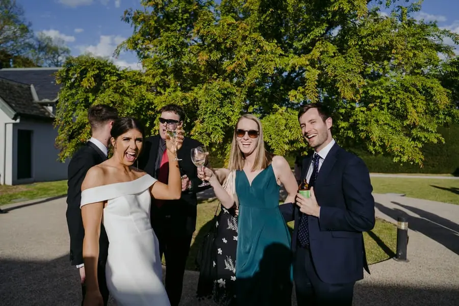 Bride and guests smiling with drinks on a sunlit lawn