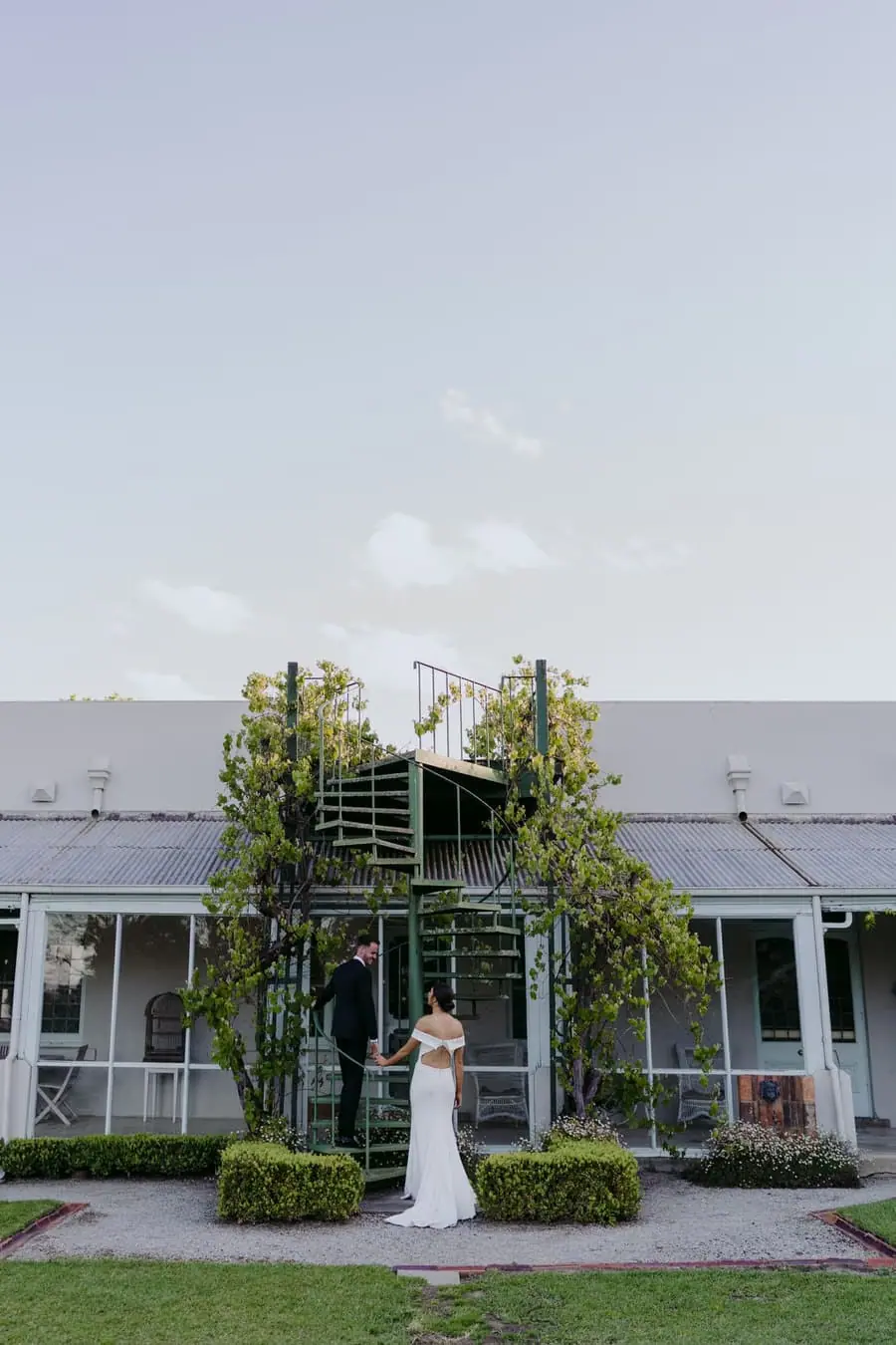 Bride standing on a vine-covered spiral staircase outside a white building