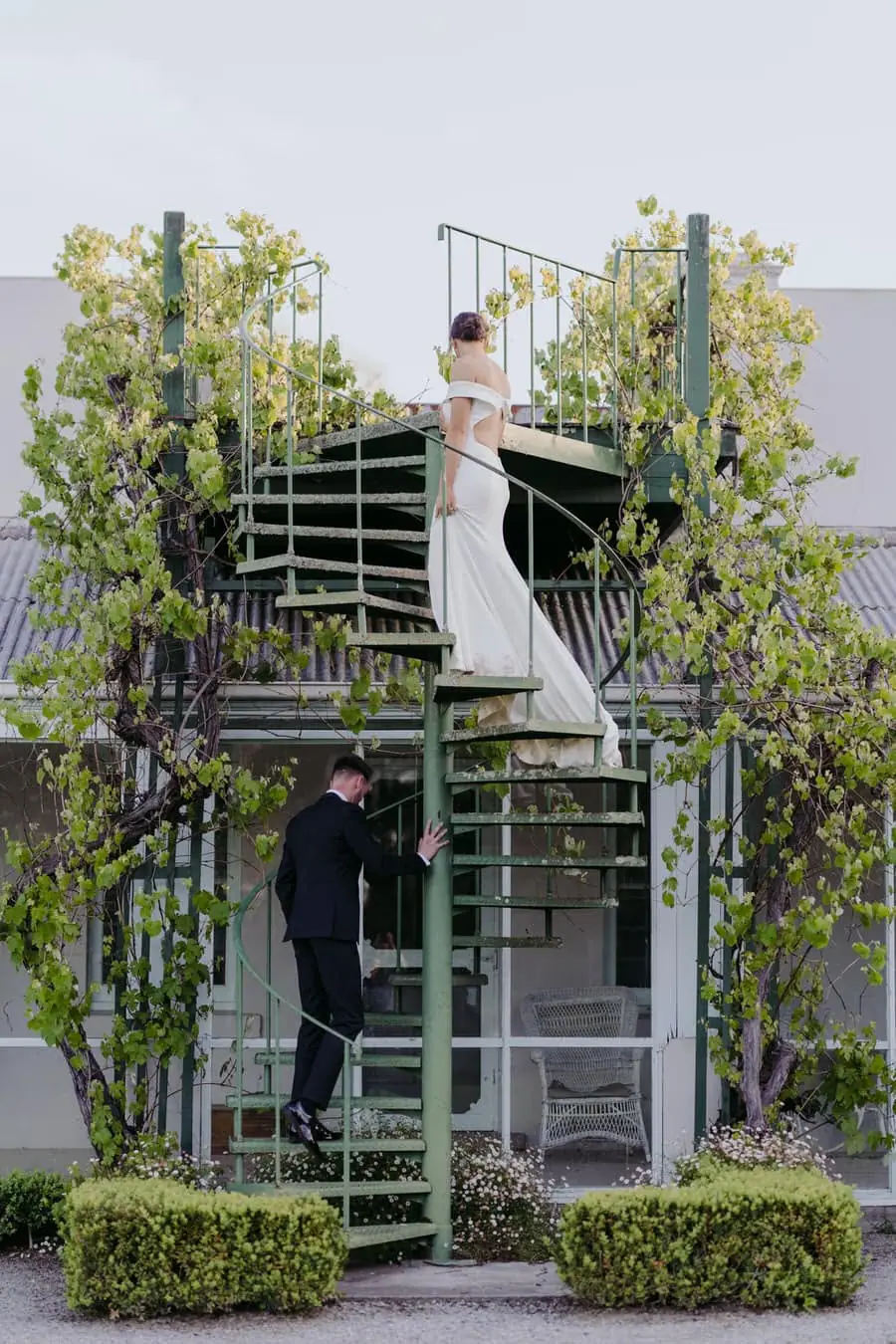 Bride standing above the groom on a green spiral staircase