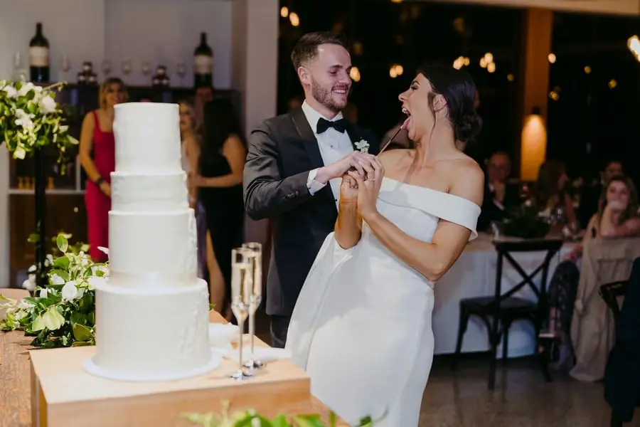 Bride and groom laughing beside a tall white wedding cake