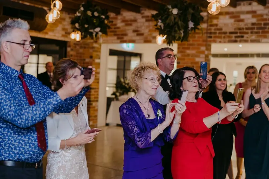 Guests applauding and recording with phones beside the reception dance floor