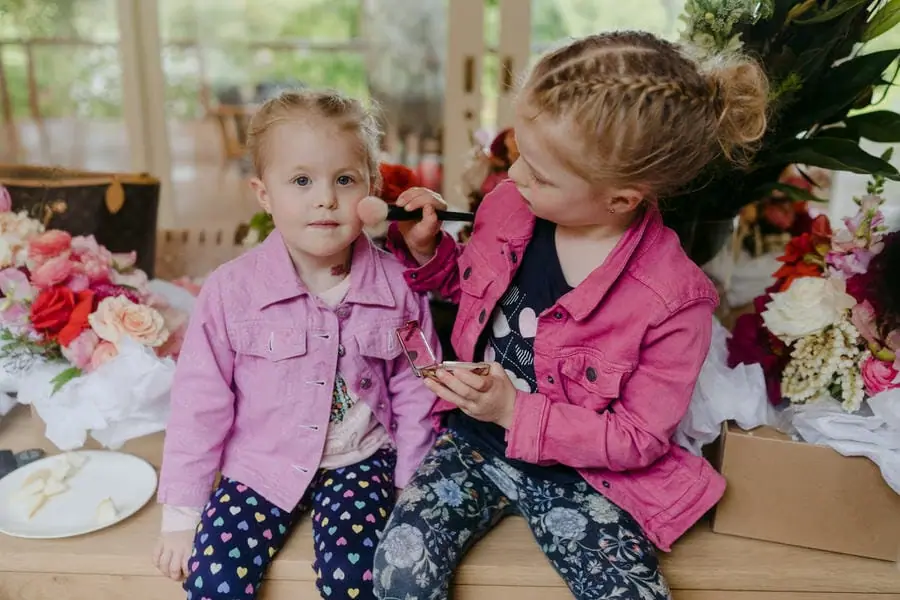 Two children in pink jackets sitting together beside wedding flowers.