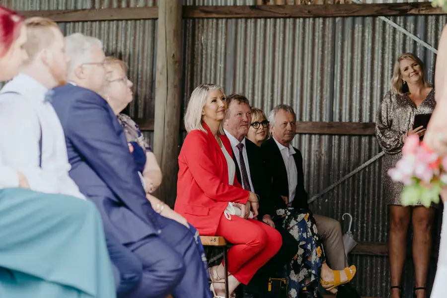 Guests seated beside a woman standing near the ceremony flowers.