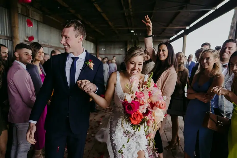 Bride and groom smiling while leaving the ceremony among cheering guests.