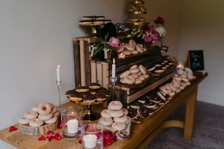 Dessert table filled with doughnuts and small cakes on wooden stands.